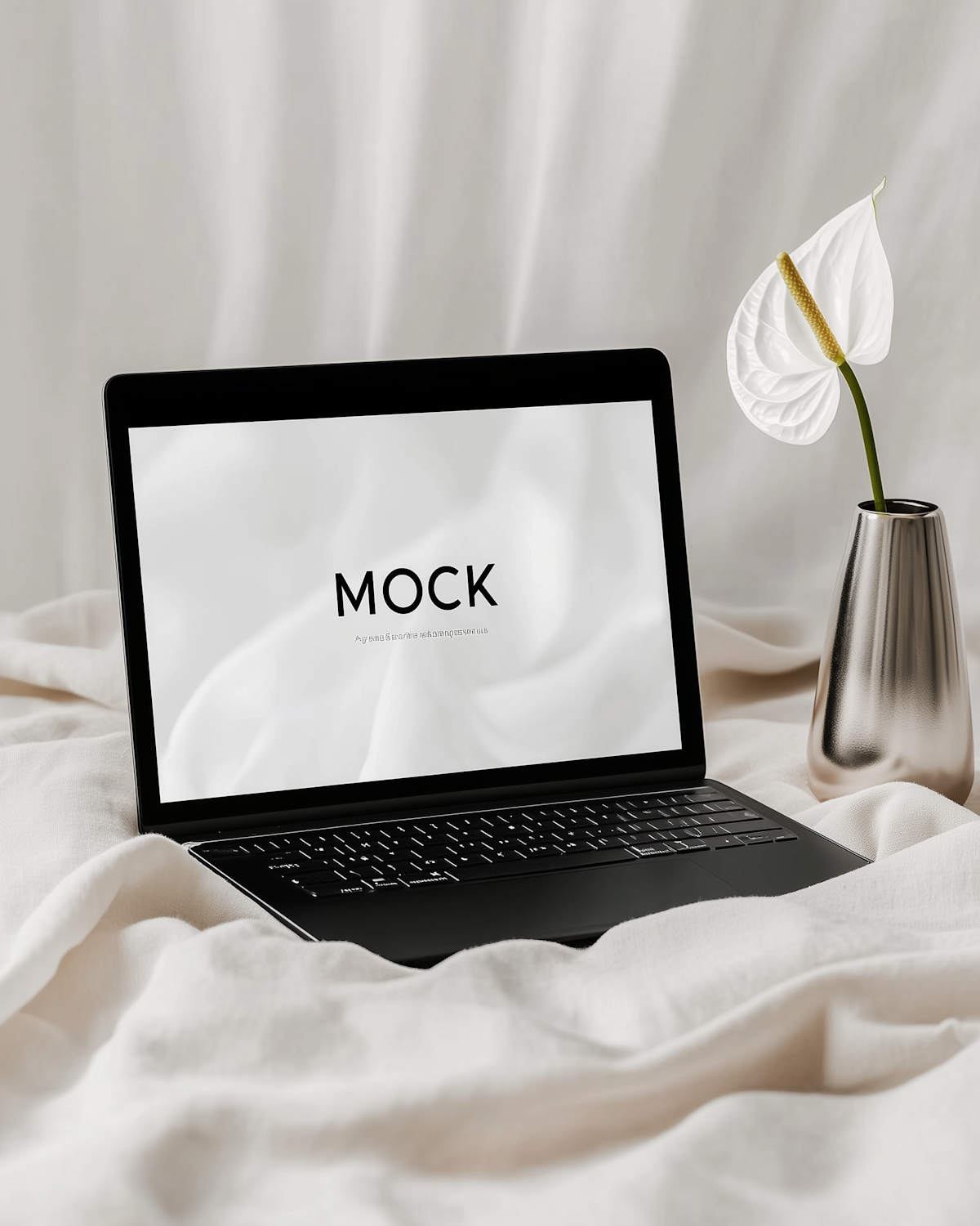 Ordinateur portable posé sur un tissu clair, à côté d'une fleur blanche dans un vase